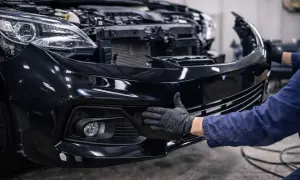 Mechanik w czarnej rękawiczce przykłada dłoń do czarnego zderzaka samochodu.