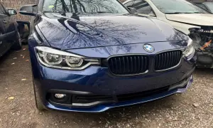 Granatowe BMW z odbiciami drzew na masce. Zastanawiasz się, ile kosztuje lakierowanie zderzaka?