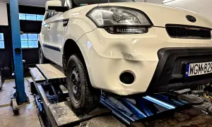Biały Kia Soul na podnośniku, przygotowany do prac, jak wyciąć otwór na hak holowniczy w dolnej części zderzaka.