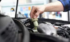 Ręka mechanika odkręca zakrętkę zbiorniczka płynu hamulcowego. Zignorowanie wymiany płynu hamulcowego powyżej 2 lat może prowadzić do awarii.