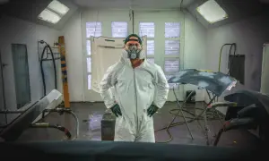 Warsztat samochodowy, gdzie można dowiedzieć się, jak usunąć rysy na nielakierowanym zderzaku strukturalnym. Pracownik w kombinezonie i masce ochronnej.