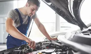 Mechanik w niebieskim kombinezonie pracuje przy silniku. Zastanawiasz się, czy warto płacić za przedłużoną gwarancję w warsztacie sieciowym zamiast u pana Mirka?