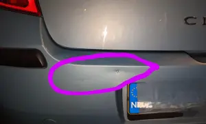 Wgnieciony plastikowy zderzak samochodu z fioletowym obramowaniem.