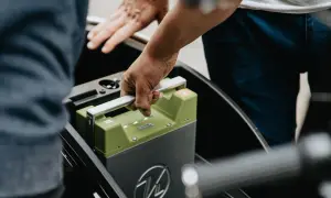 Ręce wyjmują zieloną baterię z pojazdu elektrycznego. Czy świadectwo sprawności baterii w autach EV stanie się obowiązkowe przy przeglądzie?