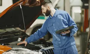 Mechanik sprawdza silnik, szukając rozwiązania, jak zamocować luźną osłonę pod silnikiem do zderzaka.