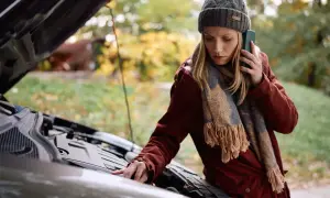 Kobieta z telefonem przy uchu sprawdza silnik auta, zastanawiając się, dlaczego nie można holować automatu.