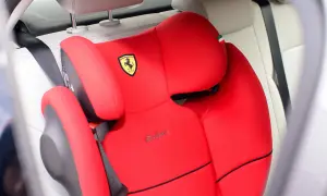 Czerwony fotelik samochodowy Cybex z logo Ferrari. Pasek bezpieczeństwa przechodzi przez fotelik, pokazując, jak prawidłowo zapinać fotelik samochodowy.