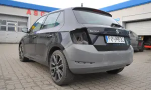 Ciemnoszara Skoda z niepomalowanym zderzakiem tył, przed warsztatem samochodowym.