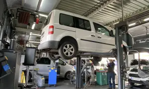 Warsztat samochodowy. Mechanik pracuje pod białym vanem na podnośniku. Prawdziwe powody dla których serwisy odmawiają montażu części dostarczonych przez klienta.