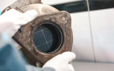 Ręce w białych rękawiczkach trzymają zardzewiały element z siatką. Może to być część procesu, jak wypalić dpf podczas jazdy.