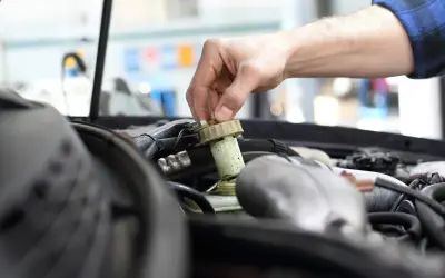 Ręka mechanika odkręca zakrętkę zbiorniczka płynu hamulcowego. Zignorowanie wymiany płynu hamulcowego powyżej 2 lat może prowadzić do awarii.