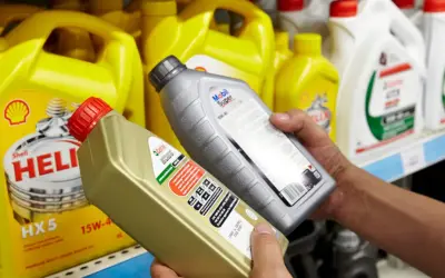 Ręce wybierają jaki olej silnikowy: Castrol EDGE i Mobil Super. W tle żółte kanistry Shell Helix.
