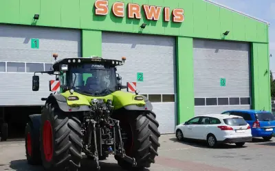 Traktor przed zielonym budynkiem serwisu. Zastanawiasz się, ile kosztuje roboczogodzina mechanika?