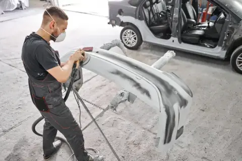 Mechanik szlifuje zderzak przed malowaniem. Dowiedz się, ile kosztuje naprawa zderzaka.