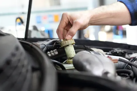 Ręka mechanika odkręca zakrętkę zbiorniczka płynu hamulcowego. Zignorowanie wymiany płynu hamulcowego powyżej 2 lat może prowadzić do awarii.