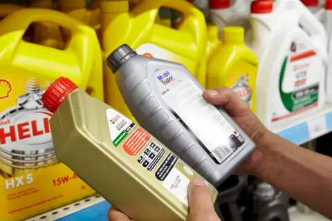 Ręce wybierają jaki olej silnikowy: Castrol EDGE i Mobil Super. W tle żółte kanistry Shell Helix.