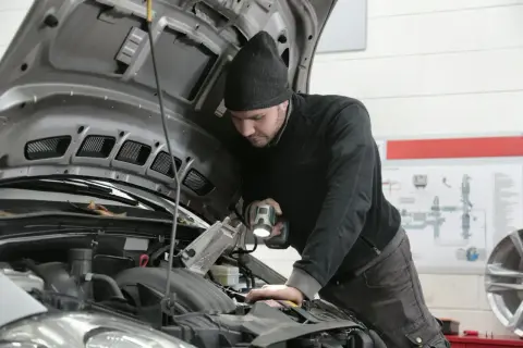 Mechanik bada przyczyny nagłego spadku mocy silnika powyżej 3000 obrotów, oświetlając silnik latarką.