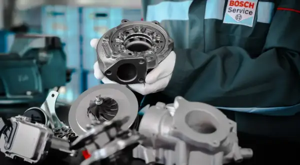 Mechanik w rękawiczkach prezentuje turbosprężarkę. Dowiedz się, jak wydłużyć żywotność turbosprężarki w silniku z start-stop.