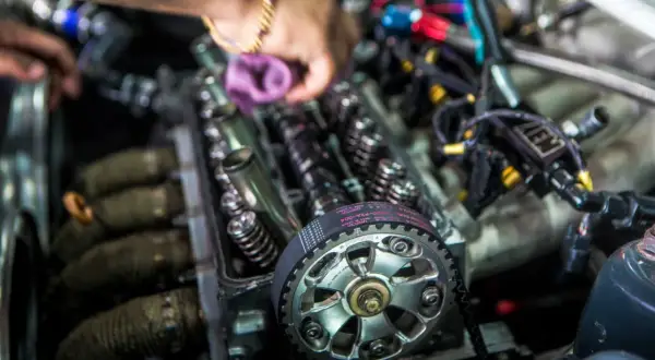 Mechanik pracuje przy silniku, pokazując różnicę między silnikiem kolizyjnym a bezkolizyjnym. Widoczny pasek rozrządu i zawory.