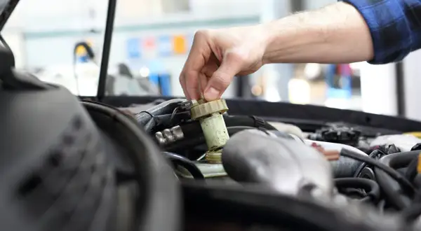 Ręka mechanika odkręca zakrętkę zbiorniczka płynu hamulcowego. Zignorowanie wymiany płynu hamulcowego powyżej 2 lat może prowadzić do awarii.