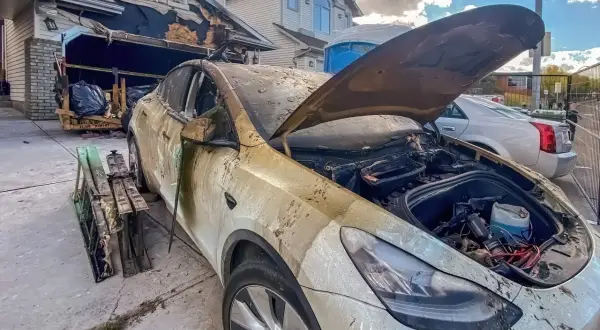 Spalony samochód elektryczny przed zniszczonym garażem. Może to być przyczyna, dlaczego w 2026 r. wzrosła liczba pożarów w warsztatach przez błędy w ładowaniu baterii.