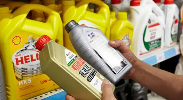Ręce wybierają jaki olej silnikowy: Castrol EDGE i Mobil Super. W tle żółte kanistry Shell Helix.