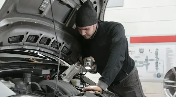 Mechanik bada przyczyny nagłego spadku mocy silnika powyżej 3000 obrotów, oświetlając silnik latarką.