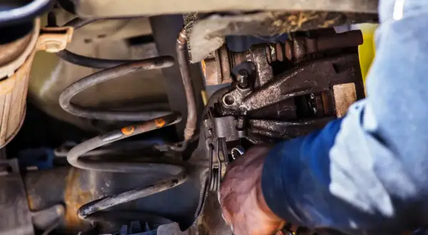 Mechanik przy pracy nad sprężyną amortyzatora. Dowiedz się, jak ścisnąć sprężynę amortyzatora domowym sposobem.