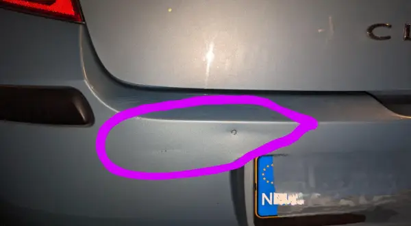 Wgnieciony plastikowy zderzak samochodu z fioletowym obramowaniem.