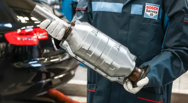 Mechanik w rękawiczkach trzyma katalizator. Usunięcie go w benzynie może wpłynąć na moc silnika, ale też na środowisko.