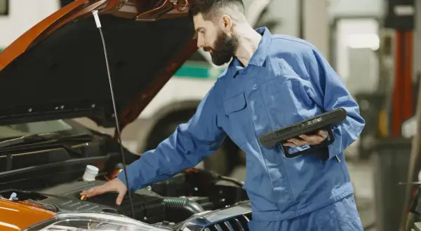 Mechanik sprawdza silnik, szukając rozwiązania, jak zamocować luźną osłonę pod silnikiem do zderzaka.