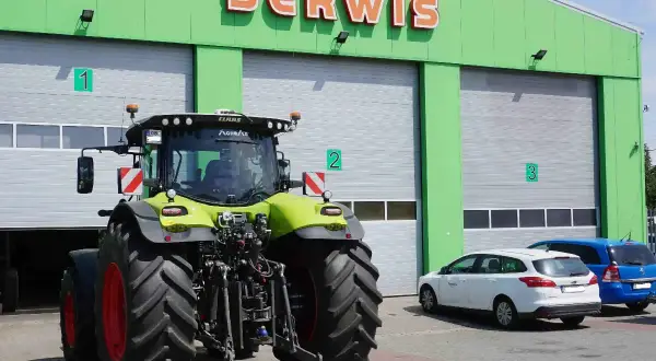 Traktor przed zielonym budynkiem serwisu. Zastanawiasz się, ile kosztuje roboczogodzina mechanika?