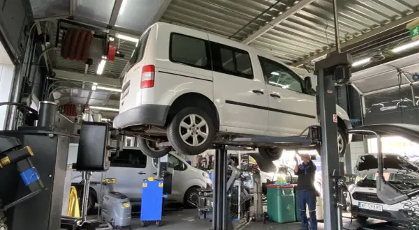 Warsztat samochodowy. Mechanik pracuje pod białym vanem na podnośniku. Prawdziwe powody dla których serwisy odmawiają montażu części dostarczonych przez klienta.