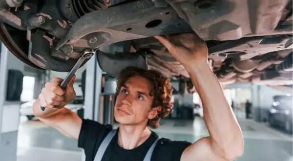 Mechanik naprawia zawieszenie, by uniknąć skutków jazdy z wybitą tuleją wahacza przedniego.