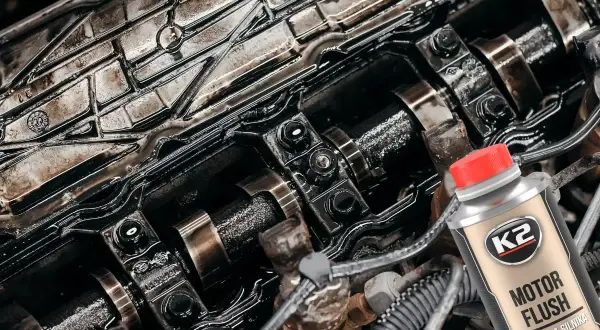 Czy płukanka silnika engine flush może rozszczelnić stary silnik? Widok wnętrza zanieczyszczonego silnika i butelki płukanki.