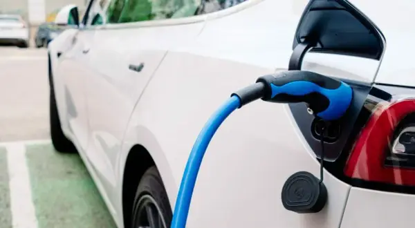Sekrety doboru opon do aut elektrycznych: dlaczego zwykłe opony niszczą się szybciej? Biały samochód elektryczny podłączony do ładowania.