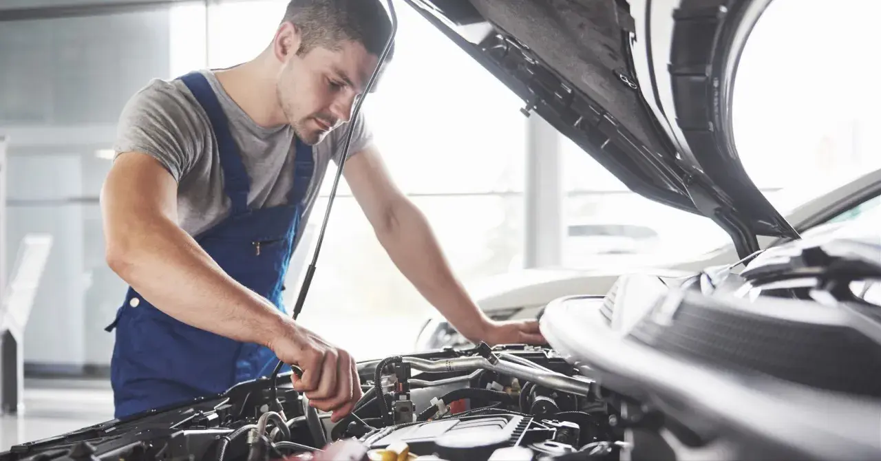Mechanik w niebieskim kombinezonie pracuje przy silniku. Zastanawiasz się, czy warto płacić za przedłużoną gwarancję w warsztacie sieciowym zamiast u pana Mirka?
