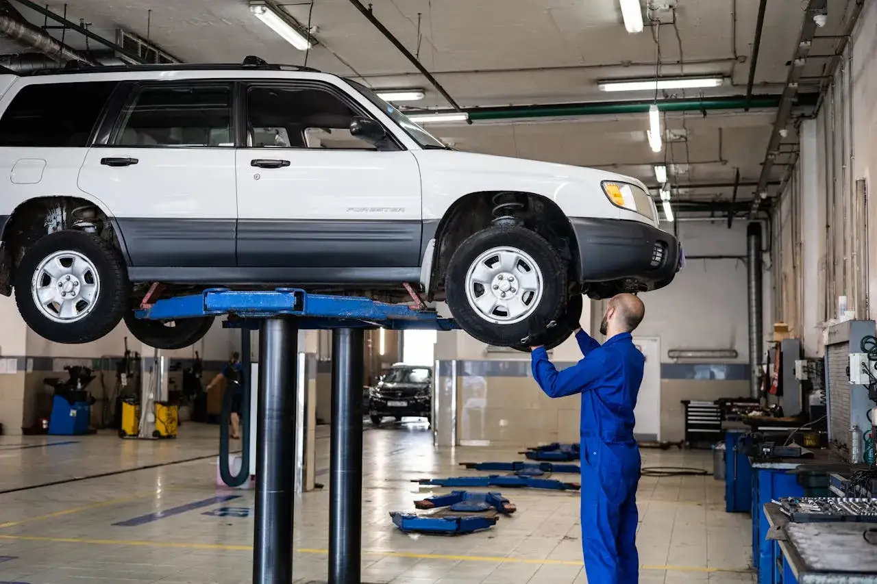 Mechanik sprawdza przednie zawieszenie po jeździe z wybitą tuleją wahacza. Auto na podnośniku w warsztacie.