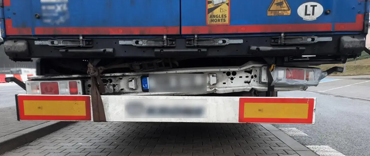 Uszkodzony zderzak ciężarówki, prowizorycznie przymocowany pasem, to niebezpieczne skutki jazdy z poluzowanym zderzakiem na autostradzie.