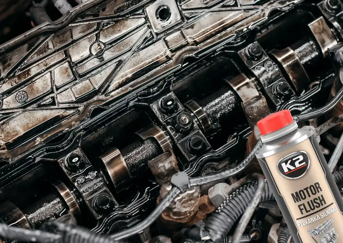 Czy płukanka silnika engine flush może rozszczelnić stary silnik? Widok wnętrza zanieczyszczonego silnika i butelki płukanki.