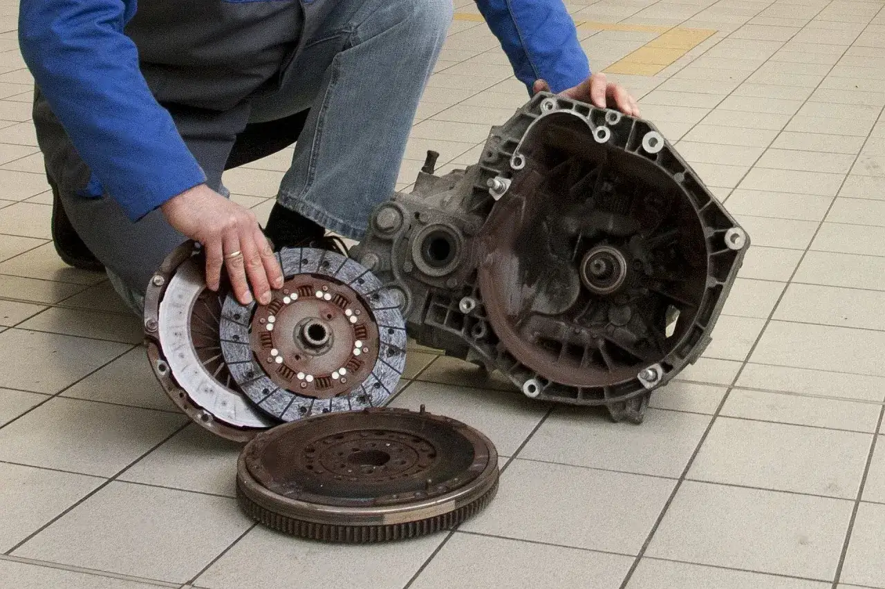 Mechanik pokazuje rozłożone części sprzęgła: koło zamachowe, tarczę i docisk. Mogą to być przyczyny hałasującego łożyska oporowego w sprzęgle.