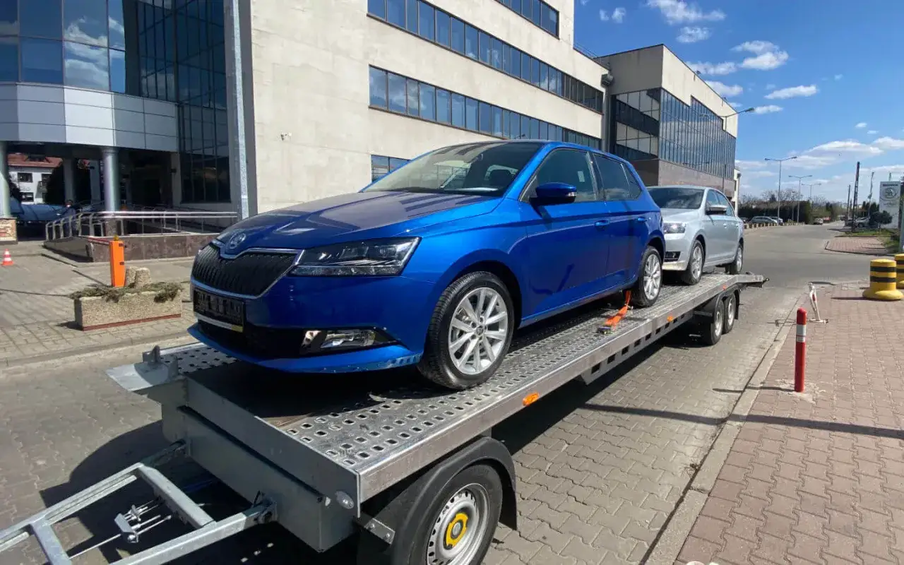Niebieska Skoda na lawecie, obok srebrny samochód. Zastanawiasz się, ile kosztuje laweta?