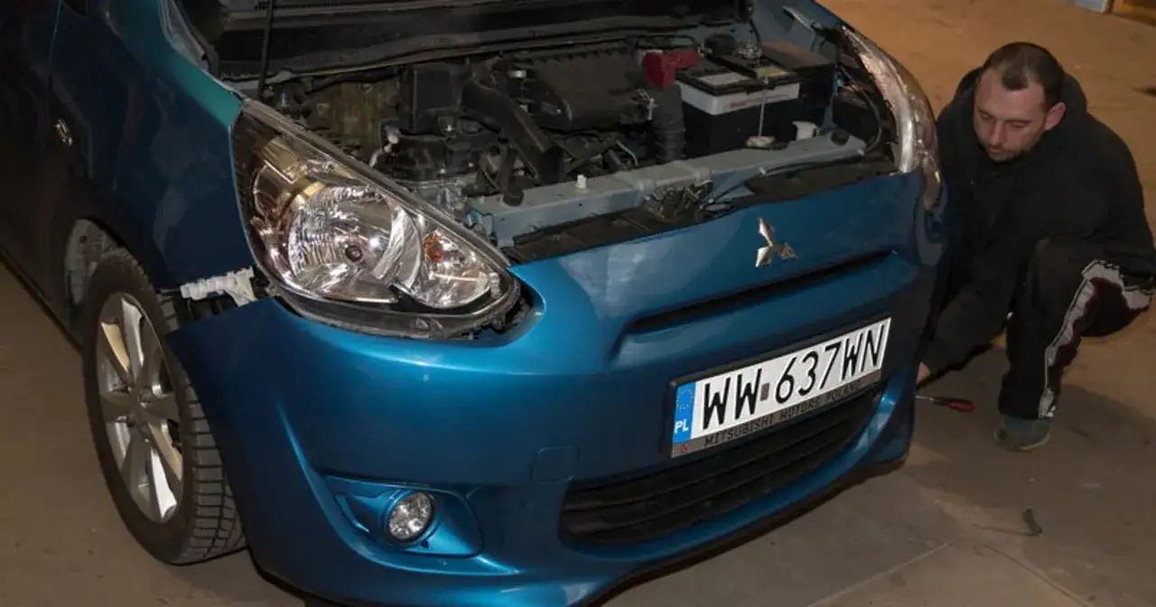 Mechanik sprawdza, czy pęknięty zderzak w niebieskim Mitsubishi przejdzie przegląd.