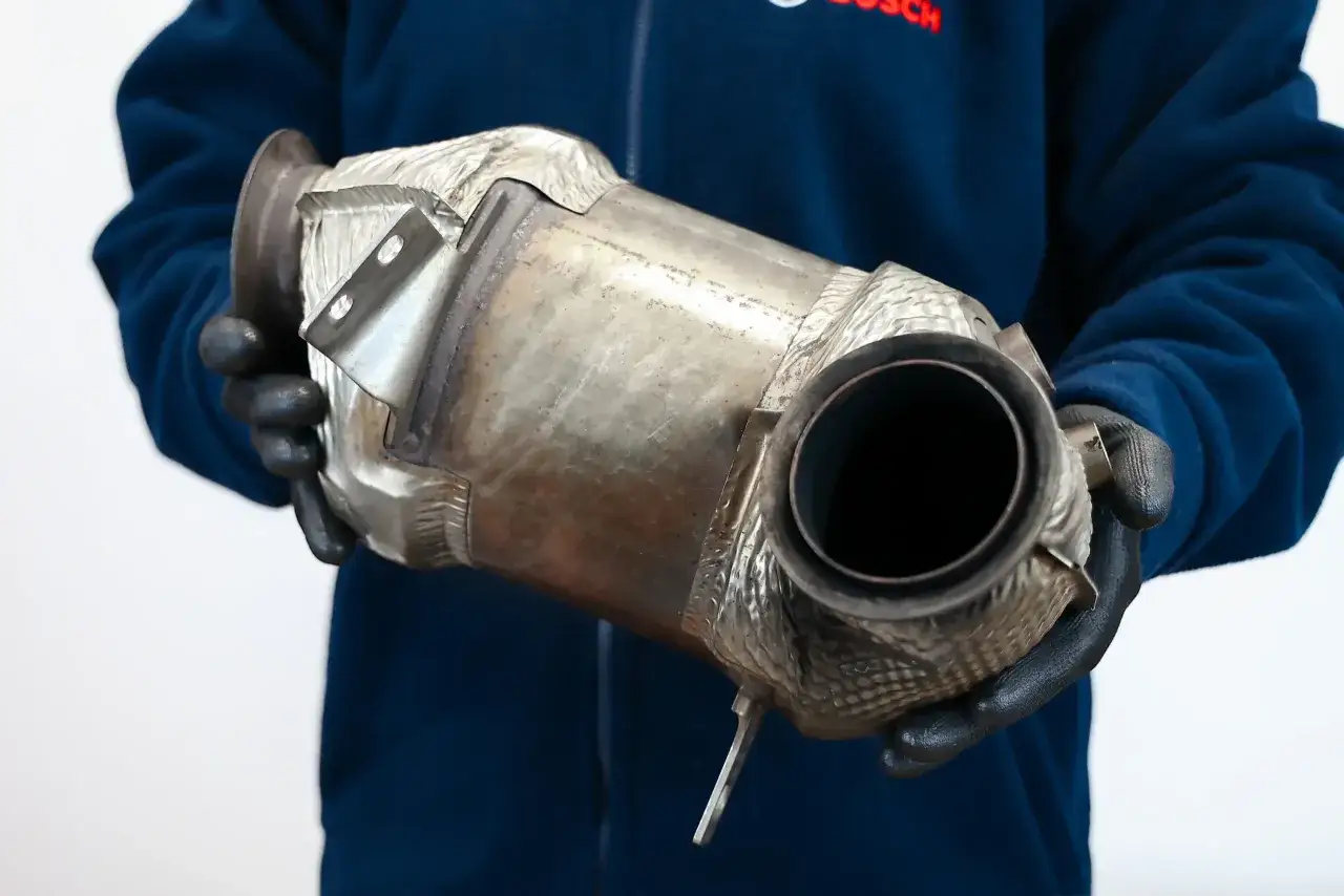 Osoba w rękawiczkach trzyma metalowy element układu wydechowego, który wygląda jak DPF. Czy mokry dpf się wypala?
