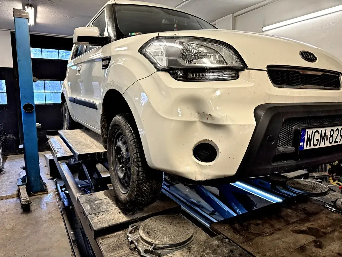 Uszkodzona belka pod zderzakiem to poważne objawy, które wpływają na bezpieczeństwo. Białe auto na podnośniku w warsztacie.