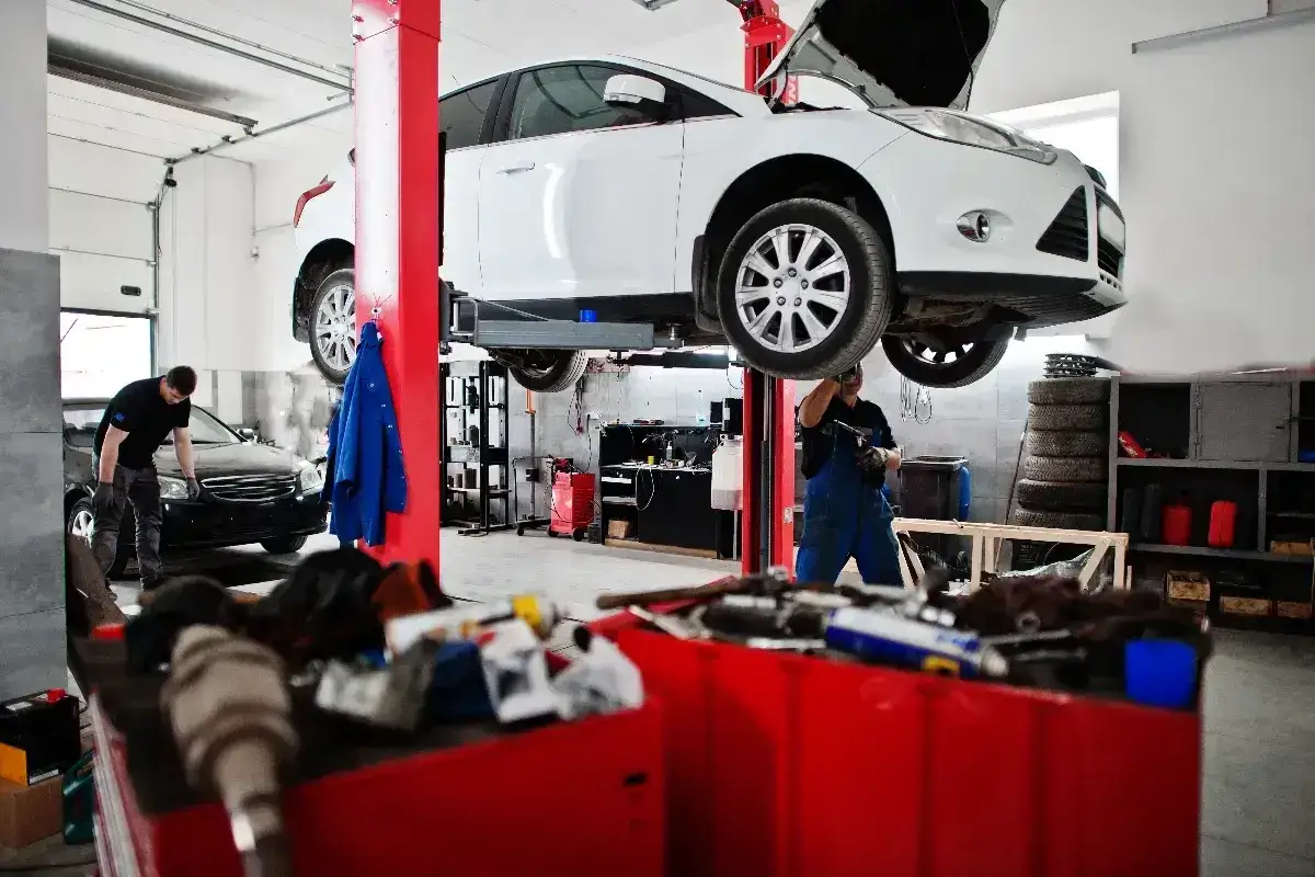 Warsztat samochodowy. Mechanik pracuje pod białym autem na podnośniku. Czy od 2026 r. warsztaty będą musiały raportować każdy wyciek płynów do bazy ochrony środowiska?