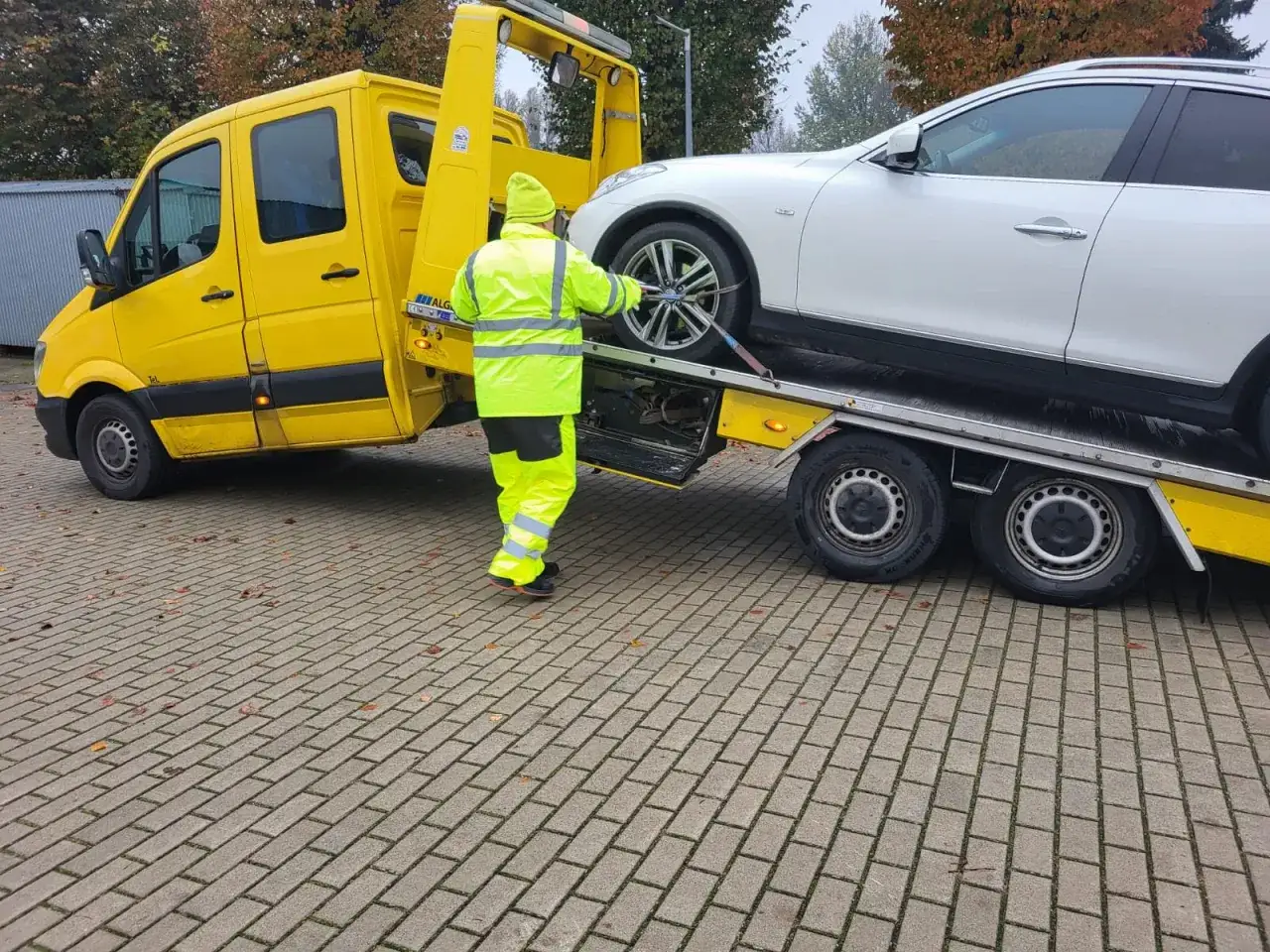 Pomoc drogowa przygotowuje białe auto do transportu. Czy można holować samochód na drodze ekspresowej? Tak, ale tylko w określonych warunkach.