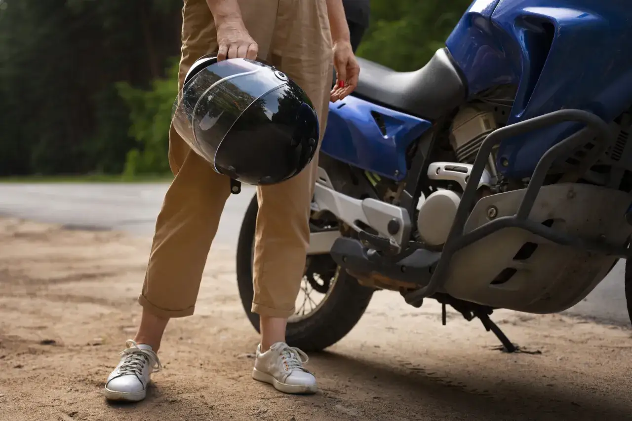 Osoba trzyma kask obok niebieskiego motocykla. Czy można holować motocykl? To pytanie może pojawić się, gdy pojazd odmówi posłuszeństwa.