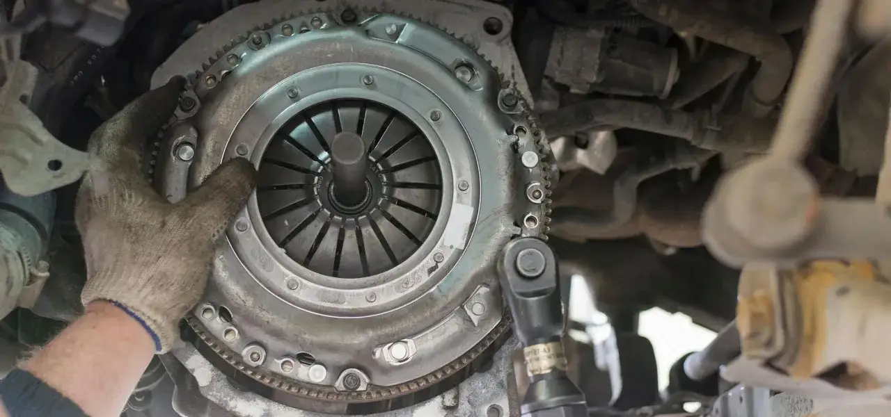 Mechanik sprawdza stan sprzęgła, by ocenić, jak rozpoznać ślizgające się sprzęgło. Widoczny mechanizm z zębatkami i tarczą.