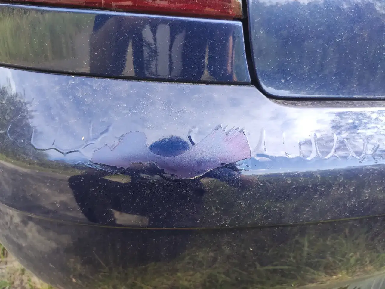 Uszkodzony lakier na granatowym zderzaku, łuszczący się płatami. Może to być efekt pękania lakieru na zderzaku przy niskich temperaturach.